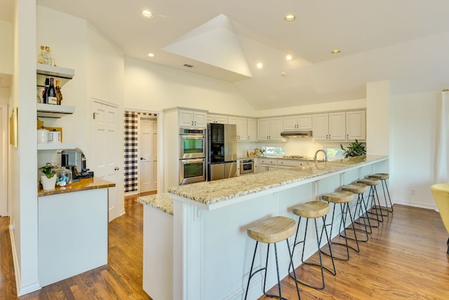 5801 Fox Chapel Dr, Austin, TX 78746 - kitchen with appliances with stainless steel finishes, a breakfast bar, light stone countertops, a peninsula, and wood finished floors