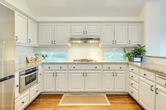 5801 Fox Chapel Dr, Austin, TX 78746 - kitchen with appliances with stainless steel finishes, under cabinet range hood, white cabinetry, decorative backsplash, and wood finished floors