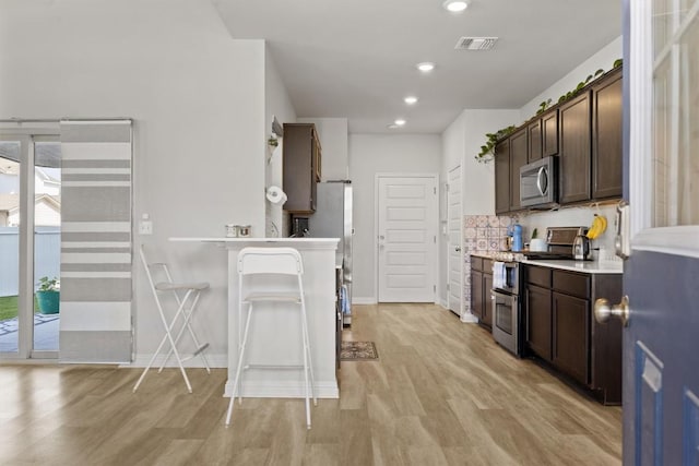 7818 Moody Bnd, Austin, TX 78744 - kitchen featuring stainless steel appliances, dark brown cabinetry, light wood finished floors, light countertops, and recessed lighting