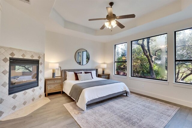 13601 Montview Dr, Austin, TX 78732 - bedroom with multiple windows, a tile fireplace, a raised ceiling, and wood finished floors