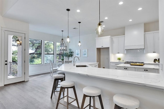 13601 Montview Dr, Austin, TX 78732 - kitchen featuring a sink, custom range hood, light wood finished floors, white cabinetry, and light stone countertops