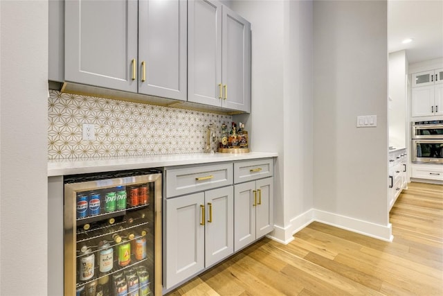 5904 Hudson Bend Rd, Austin, TX 78734 - indoor wet bar featuring beverage cooler, light wood-style floors, tasteful backsplash, stainless steel double oven, and recessed lighting