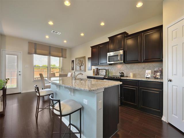 9944 Wading Pool Path, Austin, TX 78748 - kitchen with stainless steel microwave, a kitchen bar, a sink, dark wood-type flooring, and recessed lighting