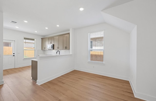 577 Tailwind Dr, Kyle, TX 78640 - kitchen featuring stainless steel microwave, light countertops, light wood-style flooring, baseboards, and a peninsula