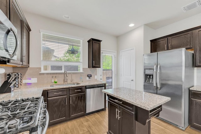 14411 Frankel Loop Unit 32B, Pflugerville, TX 78660 - kitchen with appliances with stainless steel finishes, light wood-type flooring, decorative backsplash, dark brown cabinetry, and light stone countertops