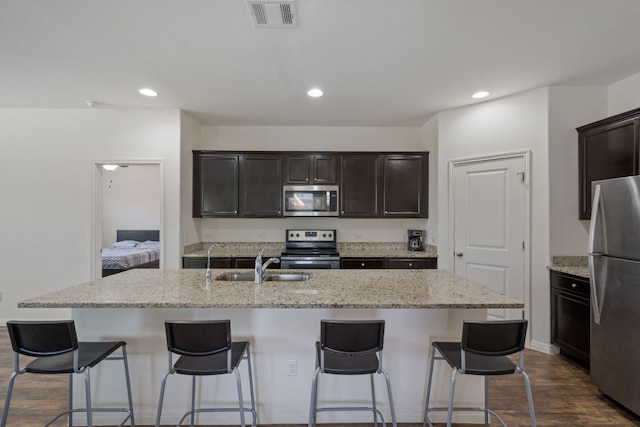13804 Mark Christopher Way, Manor, TX 78653 - kitchen featuring appliances with stainless steel finishes, a sink, an island with sink, light stone countertops, and a breakfast bar