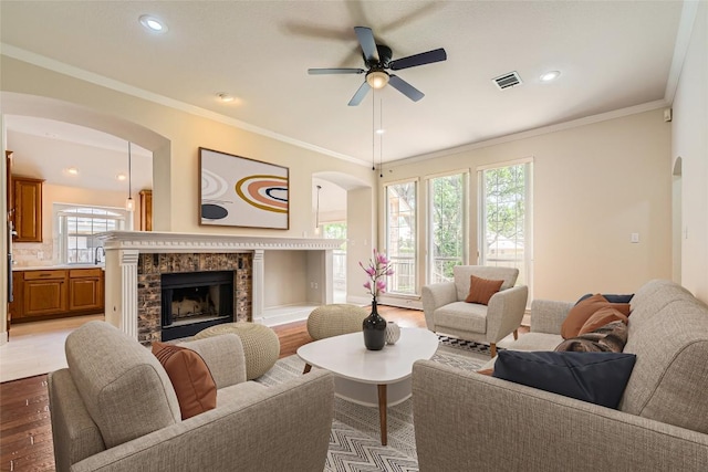 6411 Abilene Trl, Austin, TX 78749 - living room with arched walkways, light wood finished floors, a brick fireplace, a ceiling fan, and ornamental molding