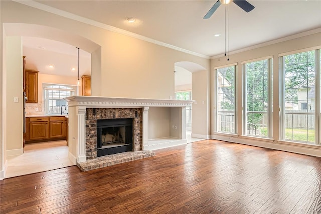 6411 Abilene Trl, Austin, TX 78749 - unfurnished living room featuring arched walkways, ceiling fan, light wood-style flooring, a brick fireplace, and ornamental molding