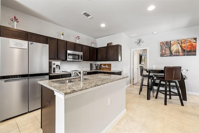 9502 Whisper Willow Blvd, Manor, TX 78653 - kitchen with appliances with stainless steel finishes, a sink, dark brown cabinetry, decorative backsplash, and light stone countertops