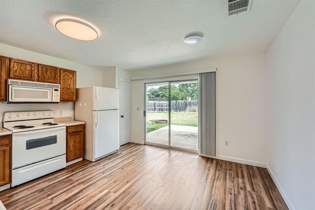 12404 Campana Dr, Del Valle, TX 78617 - kitchen featuring white appliances, brown cabinetry, light wood-type flooring, light countertops, and a textured ceiling