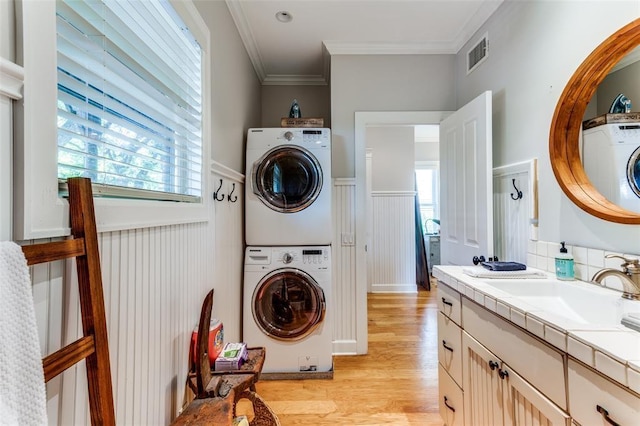 2113 Brooklyn St, Austin, TX 78704 - laundry room featuring estacked washer and dryer, wainscoting, light wood-style flooring, crown molding, and a decorative wall