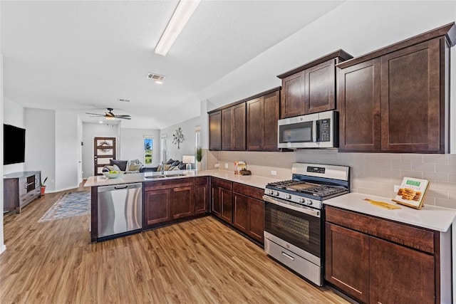 1003 Ascari Ct, Hutto, TX 78634 - kitchen with appliances with stainless steel finishes, a sink, open floor plan, dark brown cabinets, and light wood-style flooring