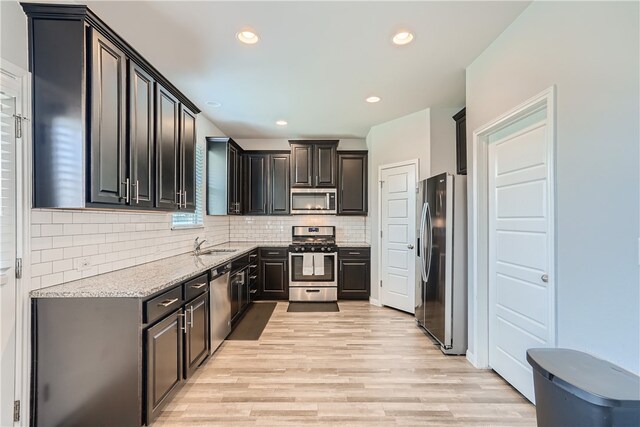 10317 Laurie Ln, Austin, TX 78747 - kitchen featuring appliances with stainless steel finishes, a sink, light stone counters, light wood finished floors, and backsplash
