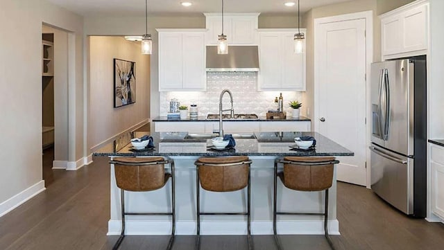 343 Jackson River Loop, Kyle, TX 78640 - kitchen featuring stainless steel refrigerator with ice dispenser, under cabinet range hood, a center island with sink, a kitchen breakfast bar, and decorative backsplash