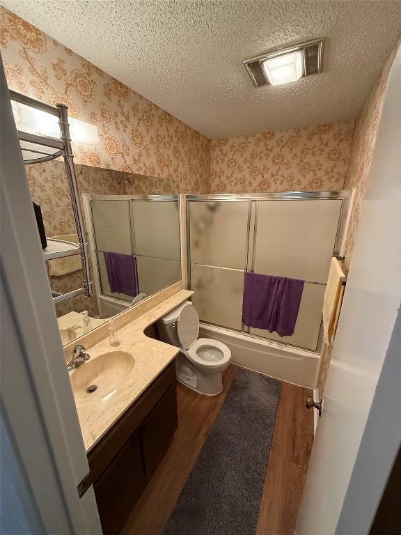 10502 Golden Meadow Dr, Austin, TX 78758 - bathroom with wallpapered walls, vanity, wood finished floors, enclosed tub / shower combo, and toilet