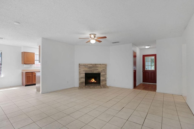 5808 Spring Meadow Rd, Austin, TX 78744 - unfurnished living room featuring ceiling fan, a textured ceiling, a brick fireplace, and light tile patterned flooring