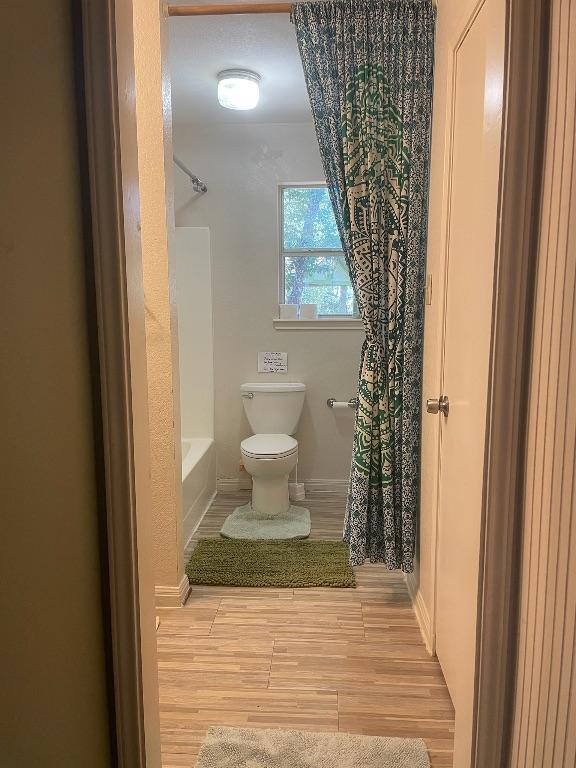 309 Stolle Ln, Flatonia, TX 78941 - full bathroom with wood finished floors, toilet, baseboards, and shower / bath combo with shower curtain
