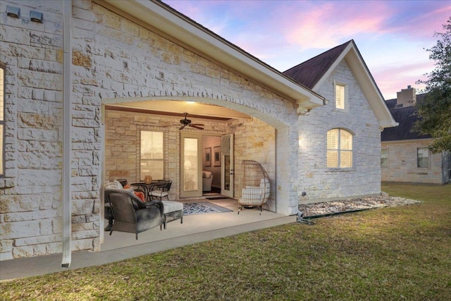 9122 Balcones Club Dr Unit 9, Austin, TX 78750 - back of house at dusk featuring stone siding, a lawn, a ceiling fan, and a patio area