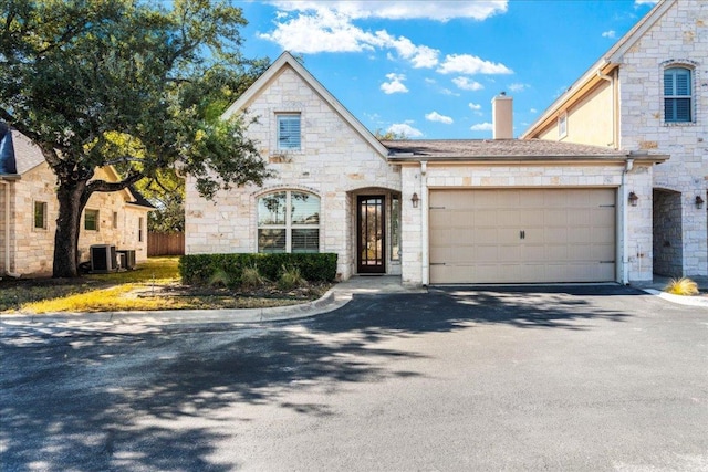 9122 Balcones Club Dr Unit 9, Austin, TX 78750 - french country inspired facade with stone siding, central air condition unit, driveway, and a chimney