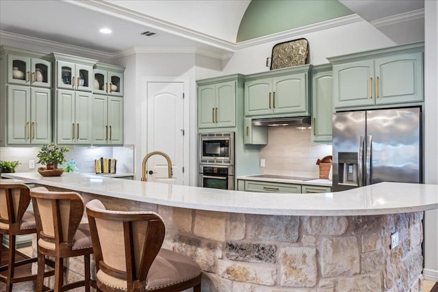 9122 Balcones Club Dr Unit 9, Austin, TX 78750 - kitchen featuring green cabinetry, stainless steel appliances, decorative backsplash, under cabinet range hood, and a kitchen bar