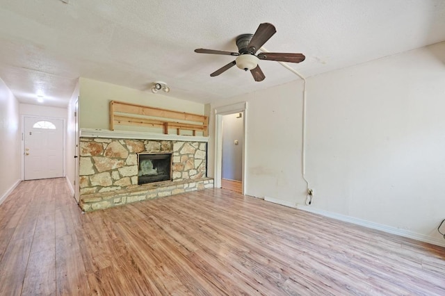 6212 Boxcar Run, Austin, TX 78745 - unfurnished living room with wood finished floors, a stone fireplace, a ceiling fan, baseboards, and a textured ceiling