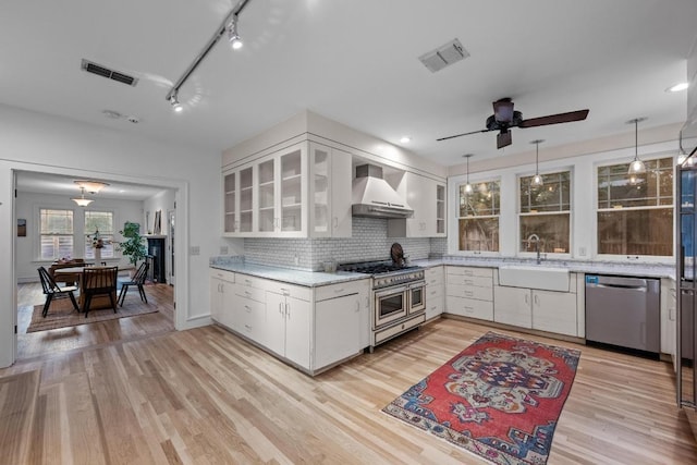 4517 Ave G, Austin, TX 78751 - kitchen with appliances with stainless steel finishes, wall chimney range hood, white cabinetry, and light wood-style flooring