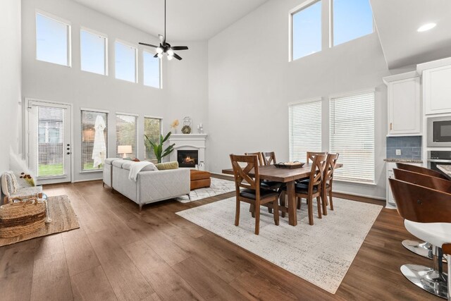 170 Fawn River Run, Kyle, TX 78640 - dining space featuring a towering ceiling, a warm lit fireplace, ceiling fan, dark wood-style flooring, and recessed lighting