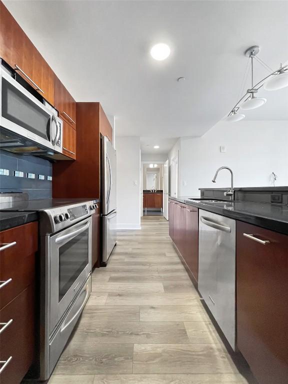 603 Davis St Unit 1108, Austin, TX 78701 - kitchen with appliances with stainless steel finishes, modern cabinets, a sink, light wood-type flooring, and dark countertops