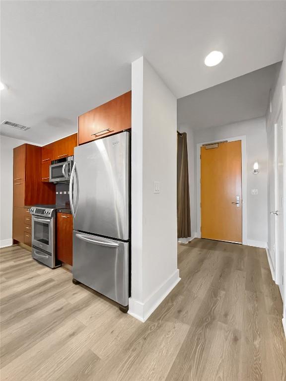 603 Davis St Unit 1108, Austin, TX 78701 - kitchen featuring stainless steel appliances, light wood-type flooring, modern cabinets, brown cabinets, and dark countertops