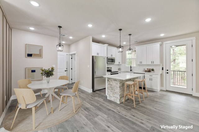 182 Kaanapali Ln, Bastrop, TX 78602 - kitchen with appliances with stainless steel finishes, a kitchen island, light countertops, light wood finished floors, and white cabinets