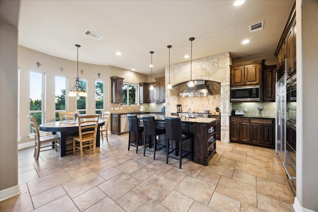613 Horseback Holw, Austin, TX 78732 - kitchen featuring stainless steel microwave, tasteful backsplash, an island with sink, wall chimney range hood, and recessed lighting