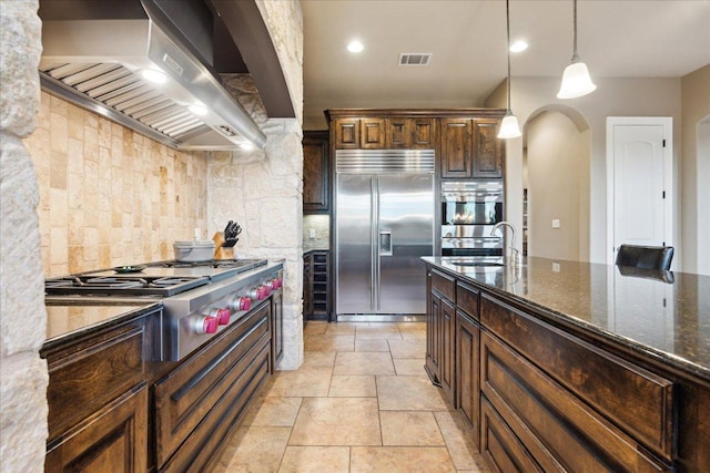 613 Horseback Holw, Austin, TX 78732 - kitchen with stainless steel appliances, wall chimney exhaust hood, arched walkways, tasteful backsplash, and pendant lighting