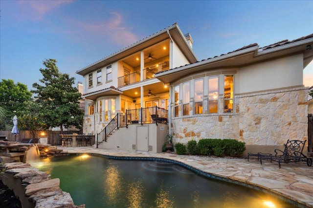 613 Horseback Holw, Austin, TX 78732 - back of house at dusk with ceiling fan, a balcony, stairs, stone siding, and a patio
