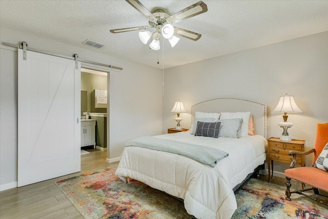 7006 Beckett Rd, Austin, TX 78749 - bedroom featuring wood finished floors, a barn door, baseboards, a textured ceiling, and a ceiling fan