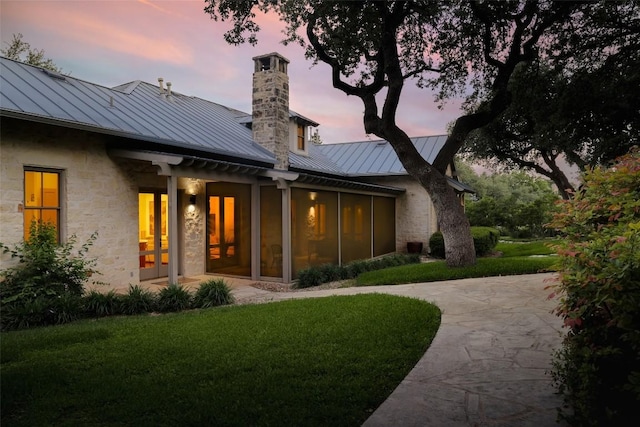 3020 Maravillas Loop, Austin, TX 78735 - back of house at dusk with a standing seam roof, metal roof, a lawn, a chimney, and a sunroom