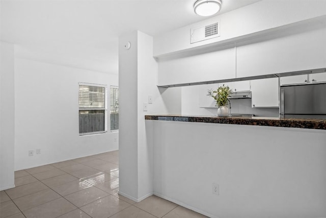 4413 Whispering Valley Dr, Austin, TX 78727 - kitchen featuring freestanding refrigerator, under cabinet range hood, light tile patterned flooring, white cabinetry, and dark countertops