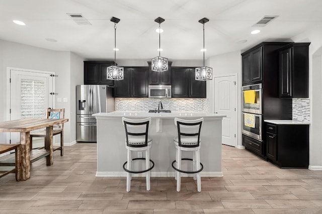 5109 Scenic Lake Dr, Georgetown, TX 78626 - kitchen with dark cabinets, stainless steel appliances, light countertops, a kitchen island with sink, and decorative backsplash