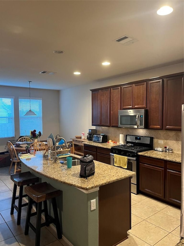 kitchen featuring appliances with stainless steel finishes, light tile patterned floors, a kitchen bar, light stone counters, and dark brown cabinets