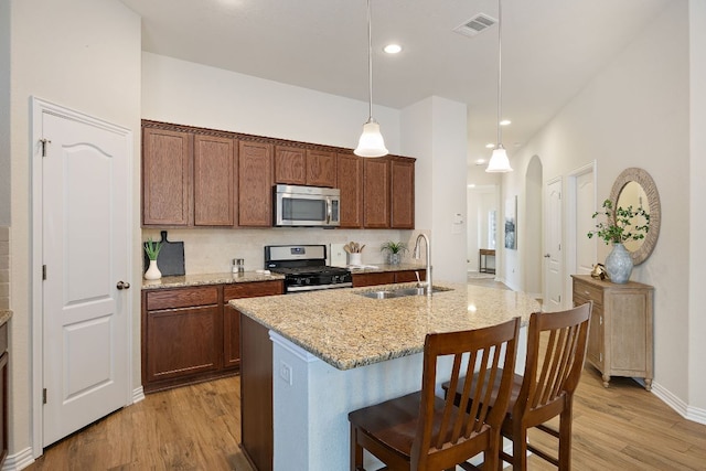 3633 Mineral Dr, Leander, TX 78641 - kitchen featuring appliances with stainless steel finishes, a sink, light wood-style flooring, a breakfast bar, and light stone counters