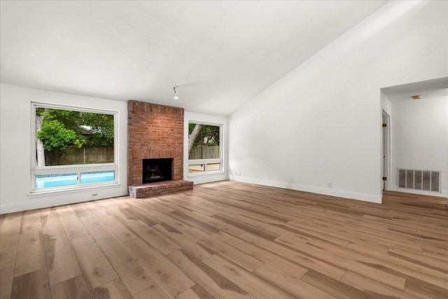 4831 Trail Crest Cir, Austin, TX 78735 - unfurnished living room featuring wood finished floors, lofted ceiling, baseboards, a brick fireplace, and rail lighting
