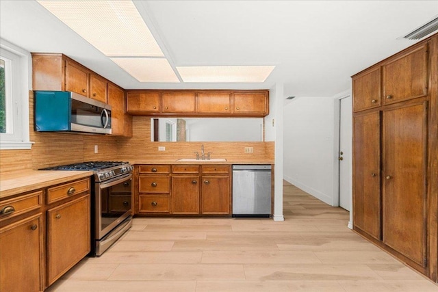 4831 Trail Crest Cir, Austin, TX 78735 - kitchen with stainless steel appliances, brown cabinetry, a sink, and light wood-style flooring