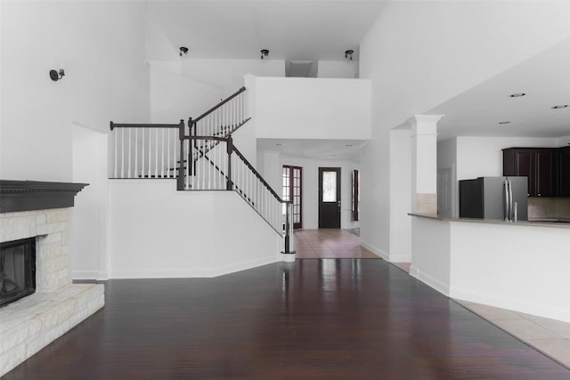 7921 Davis Mountain Pass, Austin, TX 78726 - unfurnished living room featuring wood finished floors, a high ceiling, stairway, baseboards, and a stone fireplace
