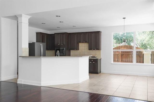7921 Davis Mountain Pass, Austin, TX 78726 - kitchen with freestanding refrigerator, light wood-style flooring, backsplash, dark brown cabinets, and a peninsula