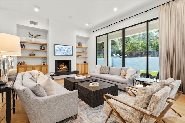 4901 Southcrest Dr, Austin, TX 78746 - living room with built in shelves, a warm lit fireplace, light wood finished floors, and recessed lighting