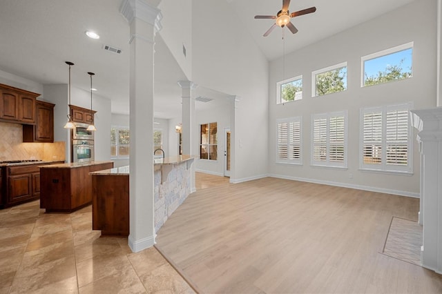12304 Buvana Dr, Austin, TX 78739 - kitchen featuring an island with sink, ornate columns, a ceiling fan, backsplash, and a high ceiling