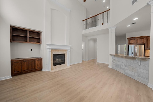12304 Buvana Dr, Austin, TX 78739 - unfurnished living room with light wood-style flooring, a fireplace with flush hearth, a high ceiling, baseboards, and decorative columns