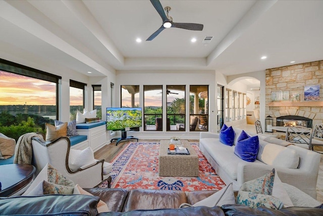921 Electra, Lakeway, TX 78734 - living room with a raised ceiling, a ceiling fan, arched walkways, light wood finished floors, and a stone fireplace