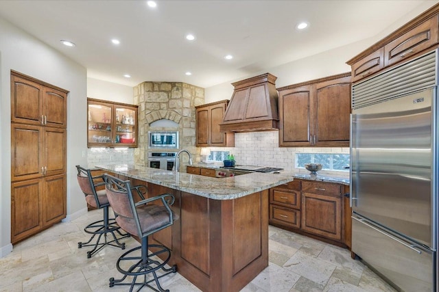 921 Electra, Lakeway, TX 78734 - kitchen featuring built in appliances, custom exhaust hood, backsplash, a center island with sink, and a kitchen bar