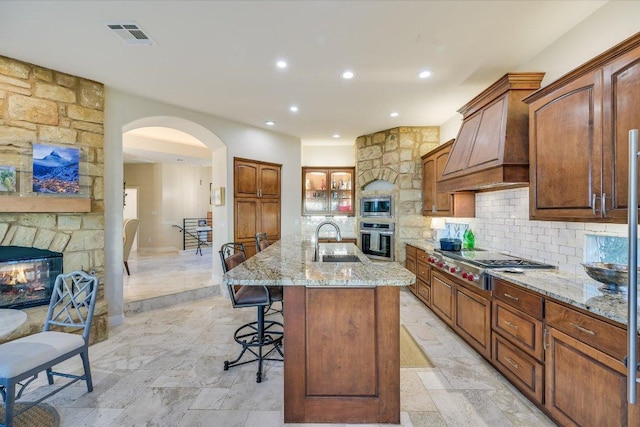 921 Electra, Lakeway, TX 78734 - kitchen featuring appliances with stainless steel finishes, a sink, light stone counters, backsplash, and a breakfast bar