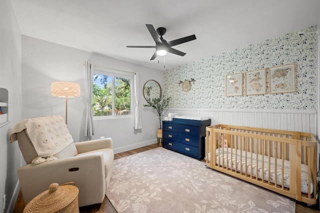 7607 Whispering Winds Dr, Austin, TX 78745 - bedroom featuring a crib, a wainscoted wall, wood finished floors, wallpapered walls, and baseboards